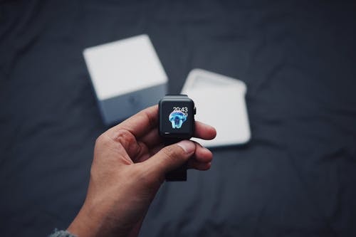 dispozitiv smartwatch Apple Watch, smartwatch in mana, cutie smartwatch pe lenjerie pat neagra