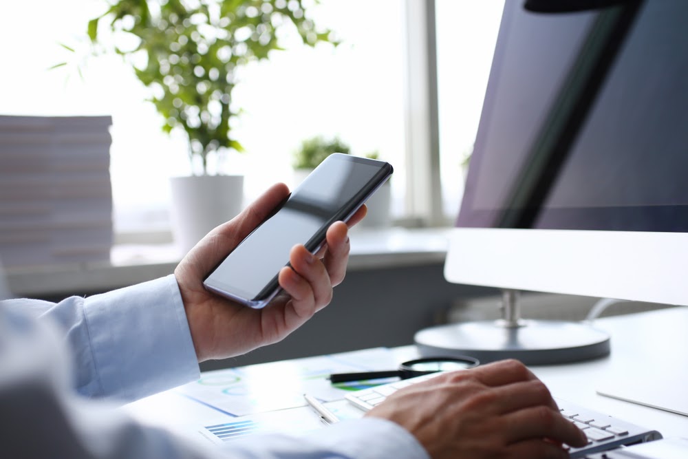 Barbat la birou cu camasa alba si smartphone in mana