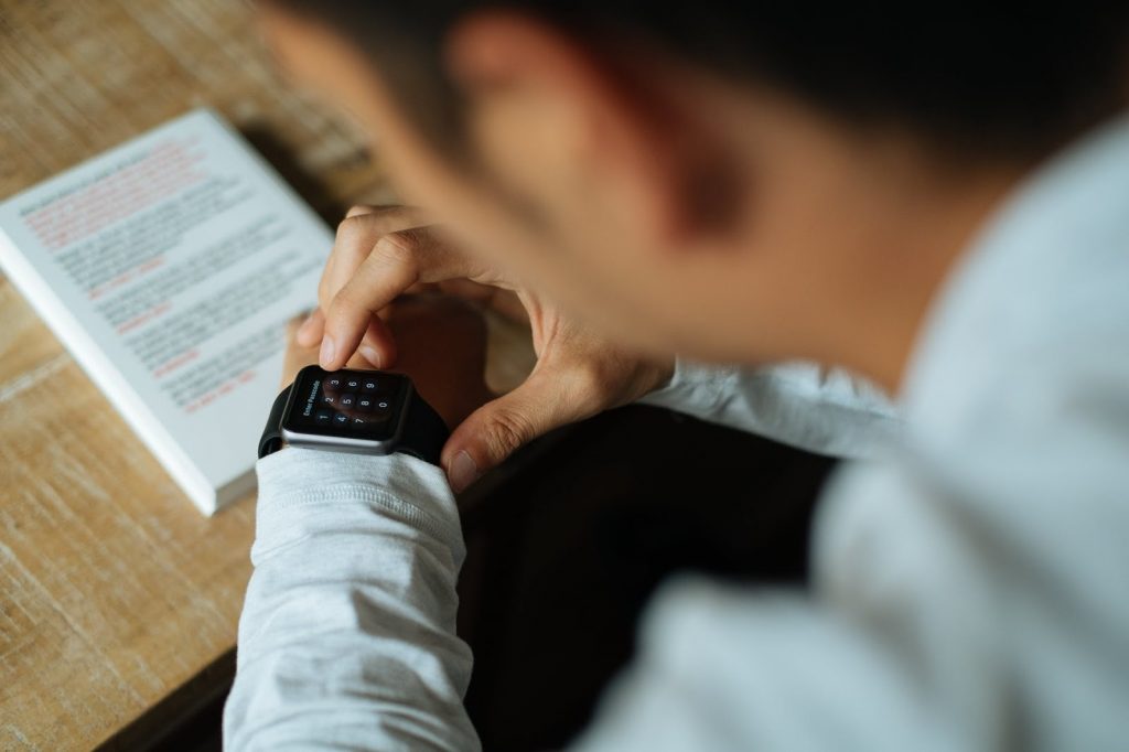 barbat purtand camasa alba si smartwatch negru, carte pe birou din lemn maro deschis