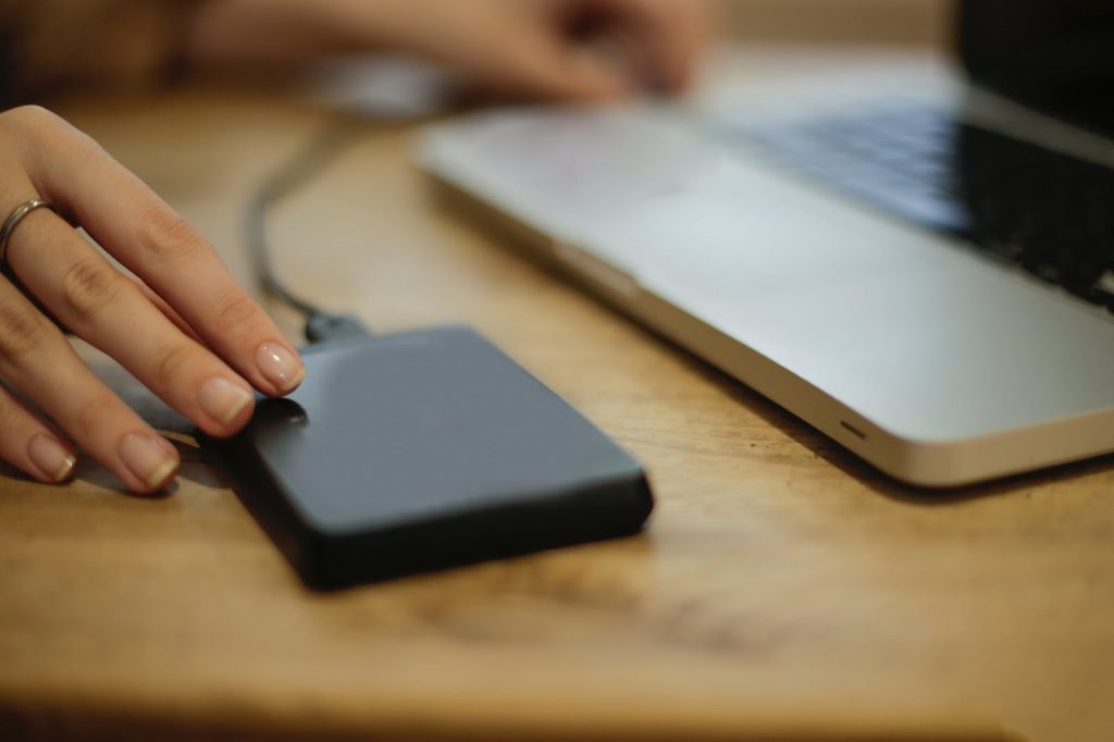 baterie externa neagra langa laptop gri, masa din lemn maro