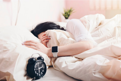 Femeie dormind cu smartwatch la mana si ceas langa